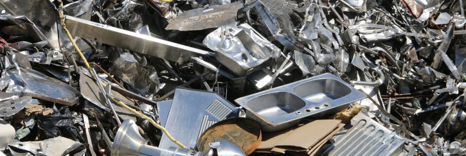 Varied metal scraps and parts piled for recycling under bright sunlight.